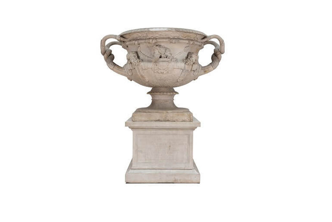 A large marble vase stands on a plinth.  The vase has handles and detailed carvings.