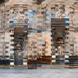 A historic, stone-built hotel in Glasgow, showing a central ornate doorway with a royal crest and a statue of a helmeted figure.