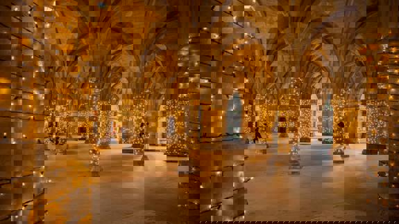 The arched stone cloister of the University of Glasgow adorned with strings of golden fairy lights in the evening.