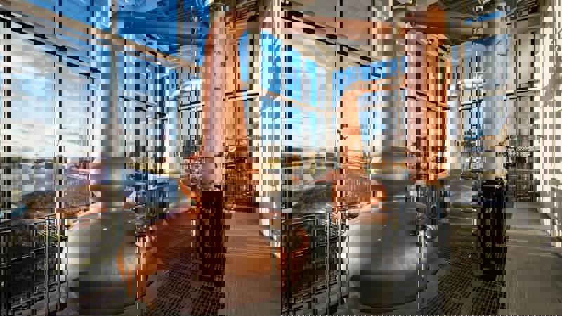 Two large copper whisky stills stand in a room with floor-to-ceiling windows overlooking the River Clyde.