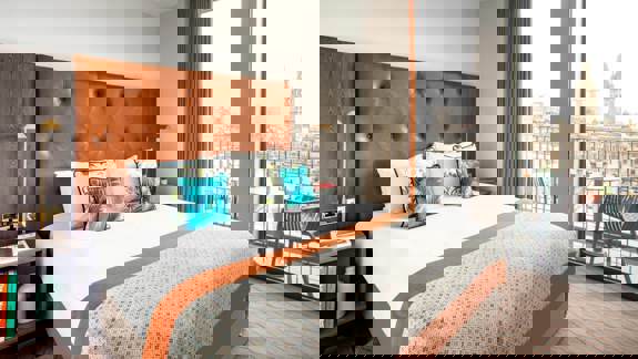 Modern apartment-style room at Native Glasgow with a king-size bed, large windows overlooking George Square, and stylish mid-century furnishings in warm tones.