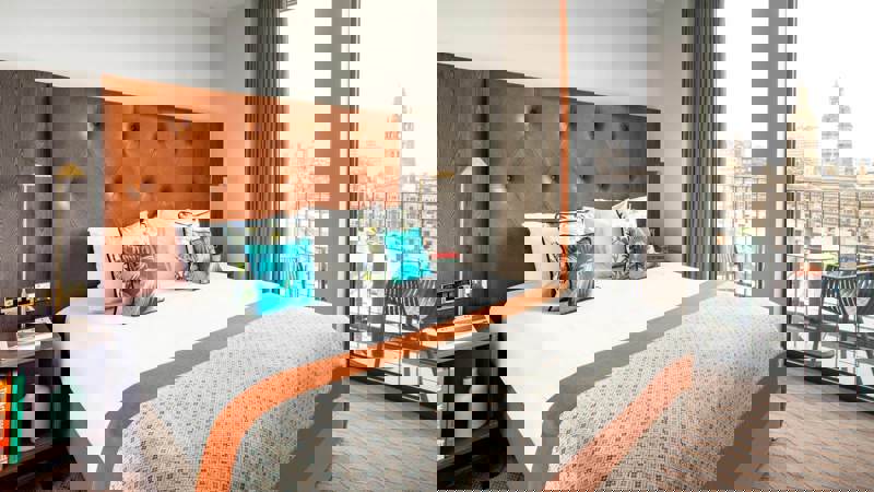 Modern apartment-style room at Native Glasgow with a king-size bed, large windows overlooking George Square, and stylish mid-century furnishings in warm tones.