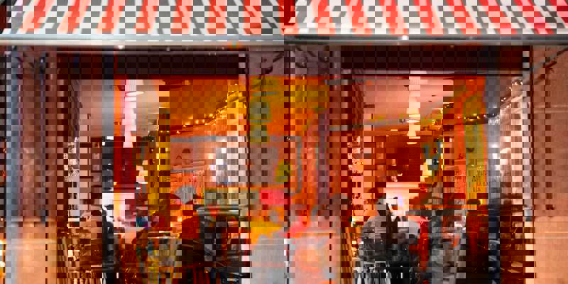 A group of people enjoying dinner inside a warmly lit Italian restaurant with a red and white striped awning.