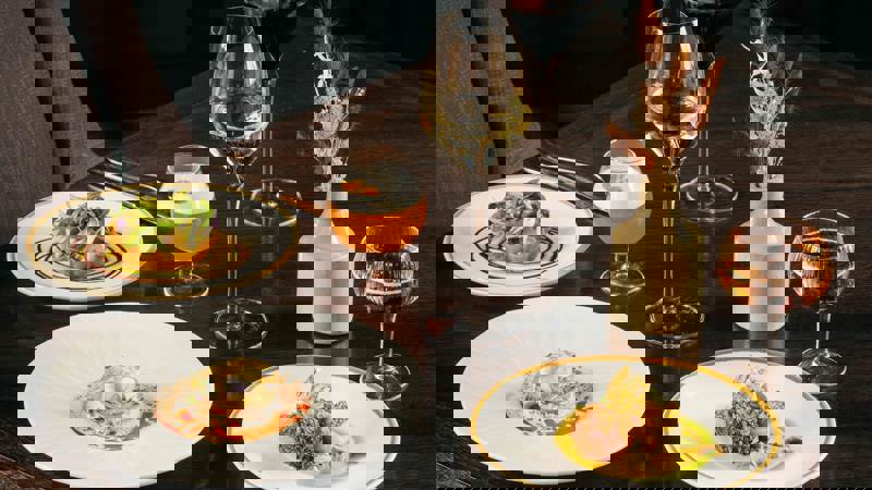 A dark wooden table set with four plates of artfully plated modern Scottish dishes, accompanied by wine and cocktails.