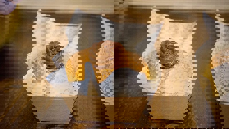 A small donut topped with a swirl of chocolate frosting sits in a paper box.