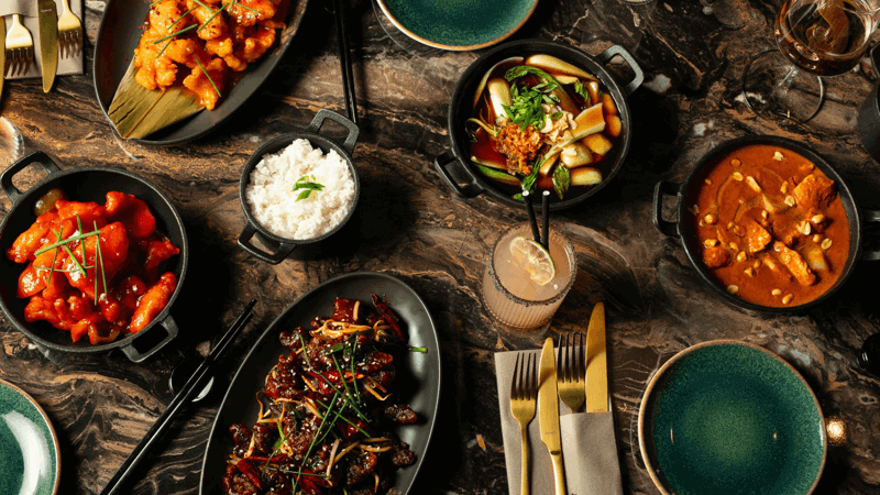 Overhead view of a variety of colourful Asian dishes, including rice, stir-fry, and curry, served on a dark marble table