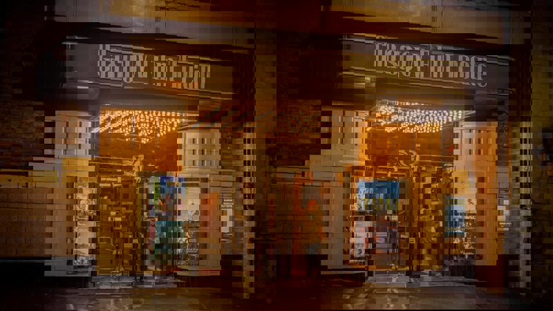 Glasgow Film Theatre exterior at night, with a person entering under a brightly lit marquee displaying movie posters.