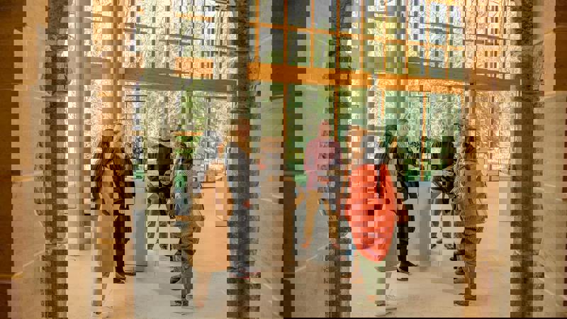 A small tour group gathers around an exhibit inside the museum, which has large windows and stone columns.
