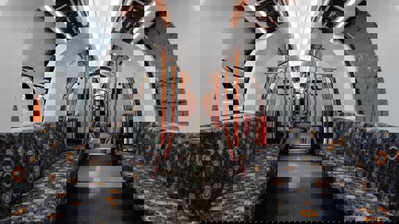 The sleek, modern interior of a Glasgow Subway train, featuring a white ceiling with orange lights and patterned grey seats.