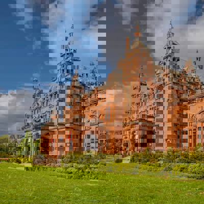 A stunning wide shot of the Kelvingrove Art Gallery and Museum, a grand red-brick building with towers and arched entryways, set against a blue sky.