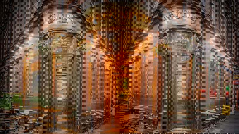 Exterior of The Ben Nevis pub on a corner street, warmly lit with wooden doors, hanging plants, and outdoor seating on the pavement.