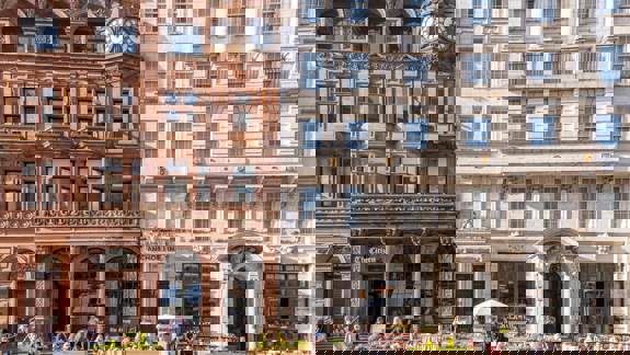 Two grand historic buildings side-by-side in Glasgow's city centre, Anchor Line and The Citizen, with outdoor dining areas bustling with people.