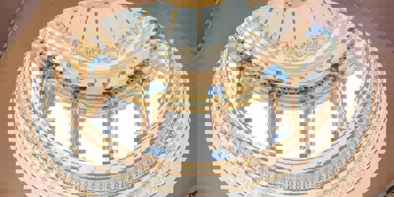 A detailed view of an ornate, circular domed ceiling with gilded, lion-like statues and decorative patterns. The dome lets in natural light.