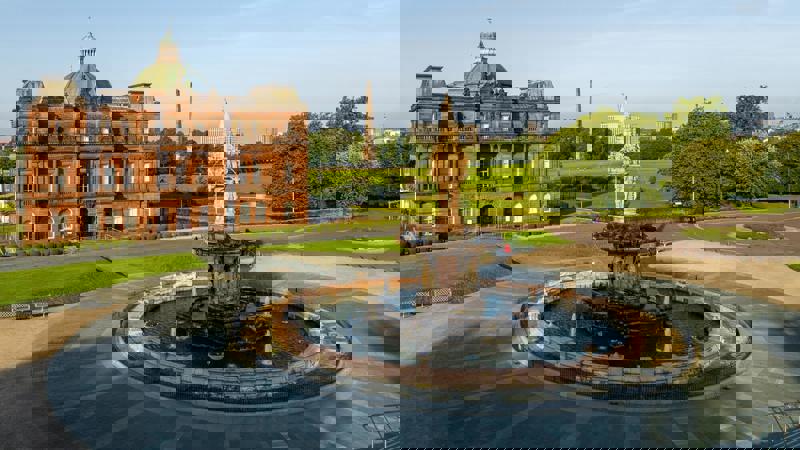 An aerial view of the Doulton Fountain in Glasgow Green with a grand building and park in the background.