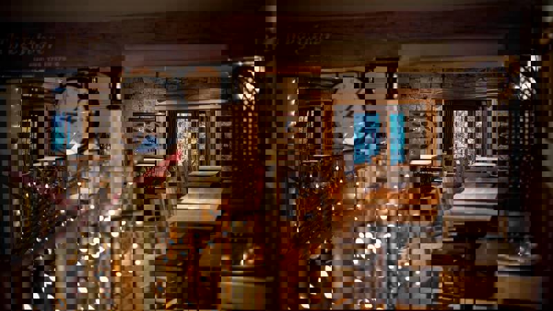 Interior of Stravaigin restaurant with warm lighting from fairy lights and windows, wooden tables and chairs, and a prominent clock, suggesting a cosy, rustic feel.