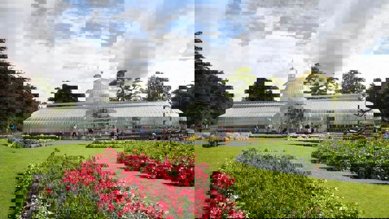 A wide shot of the Kibble Palace glasshouse in Glasgow's Botanic Gardens on a sunny day.