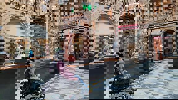 A person in a wheelchair inside the main hall of the Kelvingrove Art Gallery and Museum, with sculptures and a grand staircase in view.