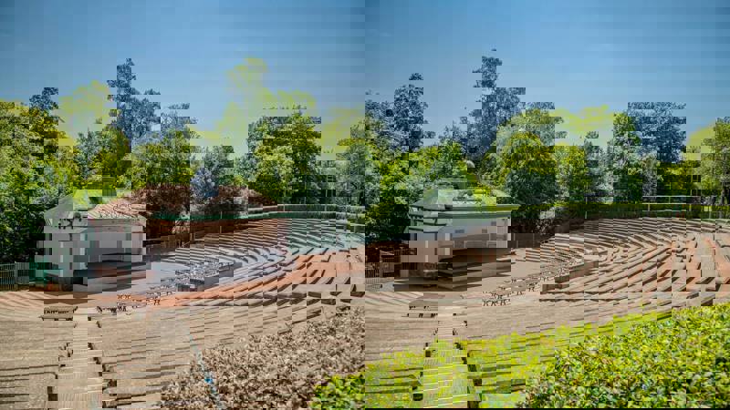 Tiered seating and stage at Kelvingrove Bandstand on a sunny day, with trees in the background.