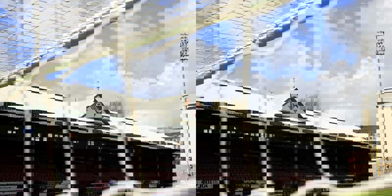 The stadium stands of a football ground are seen through the white netting of a goal. The main stand has a white roof with a triangular logo.