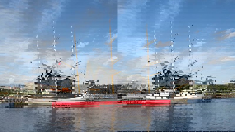 The historic tall ship Glenlee moored on the River Clyde with the modern, zig-zag roof of the Riverside Museum behind it.