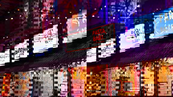 A vibrant food market at night with neon signs for various food vendors, including "Smashed Burgers" and "Pasta, Baby."