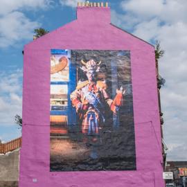 Bright pink building with a large mural of Billy Connolly in a fantastical, colourful costume with a horned helmet.